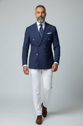 Man in navy double-breasted suit set with white tailored trousers and brown shoes.